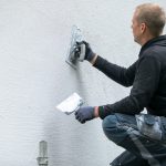 Mężczyzna nakłada dekoracyjny tynk elewacyjny na fasadę domu