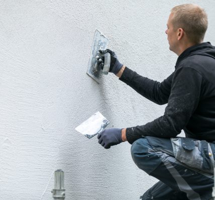 Mężczyzna nakłada dekoracyjny tynk elewacyjny na fasadę domu