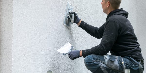 Mężczyzna nakłada dekoracyjny tynk elewacyjny na fasadę domu
